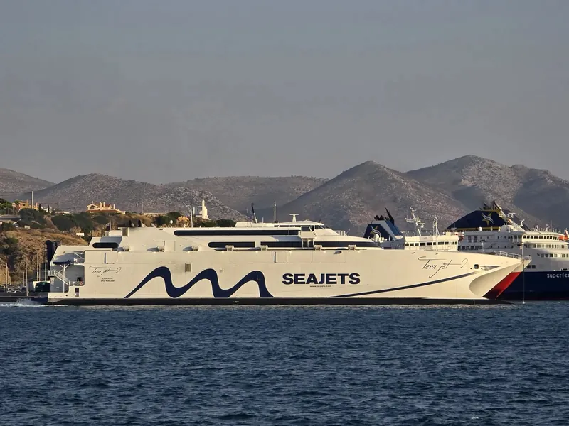 A white high-speed catamaran ferry moored in front of a larger navy and white conventional ferry