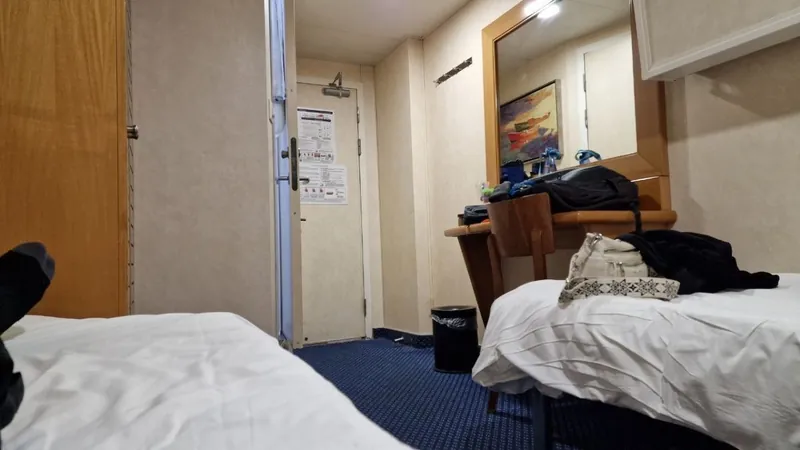 A twin-bed ferry cabin with a wooden wardrobe, dressing table, mirror and blue carpet