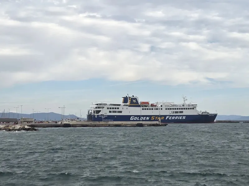 A ferry moored at a harbour wall beyond choppy grey-green water under a heavily clouded sky