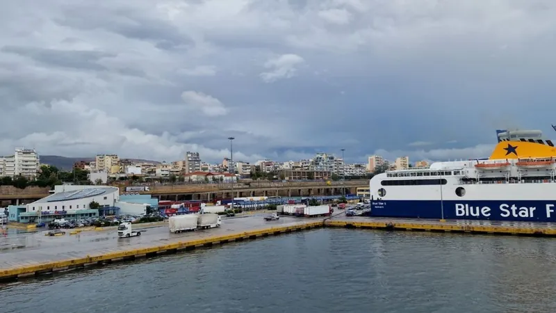 A large blue and white ferry berthed at a quiet port quay under heavy grey clouds, with lorries parked nearby