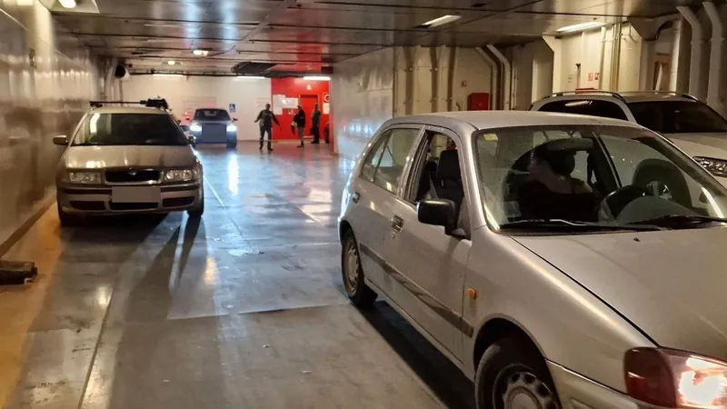 Cars parked in lanes on the vehicle deck of a ferry, with people walking in the background