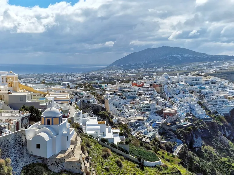 Fira town cascading down the caldera cliff on Santorini, seen from above on a cloudy day