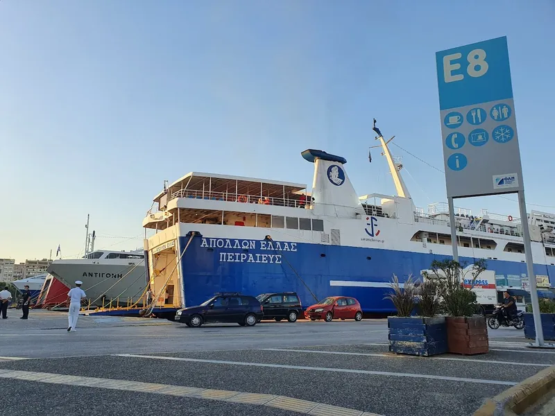 A blue and white ferry moored beside a gate E8 sign, with cars and a crew member nearby