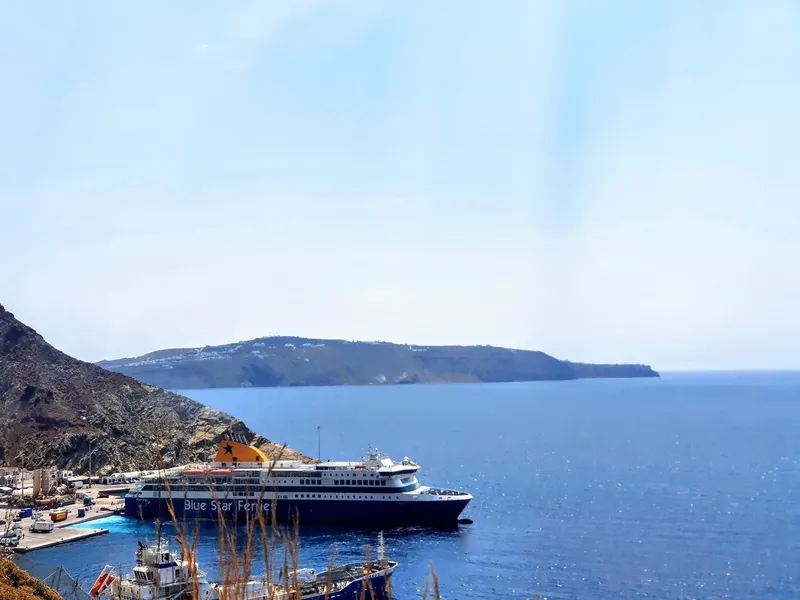 A Blue Star Ferries ship moored at Athinios port on Santorini beneath dark volcanic cliffs