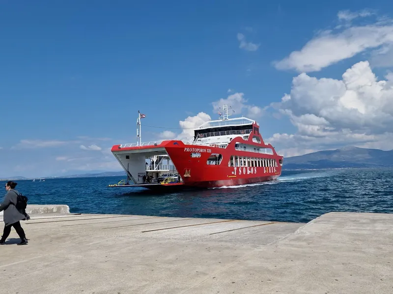 A red double-ended car ferry approaching a concrete quay on a bright blue day